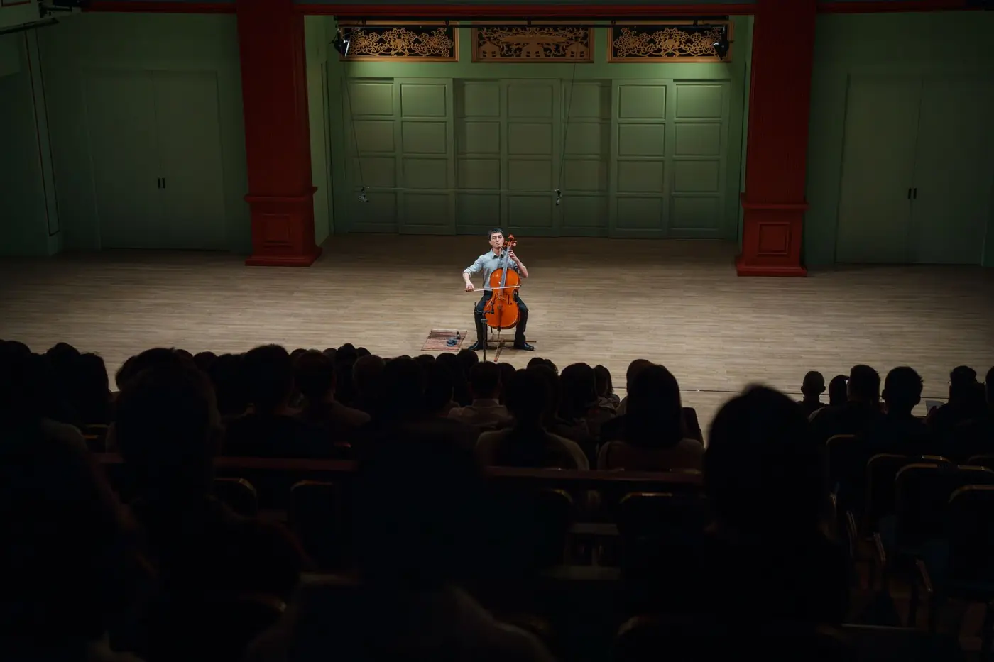 蘇炯睿醫師於音樂廳演出巴哈無伴奏大提琴組曲，舞台聚光燈下獨奏，台下觀眾滿座